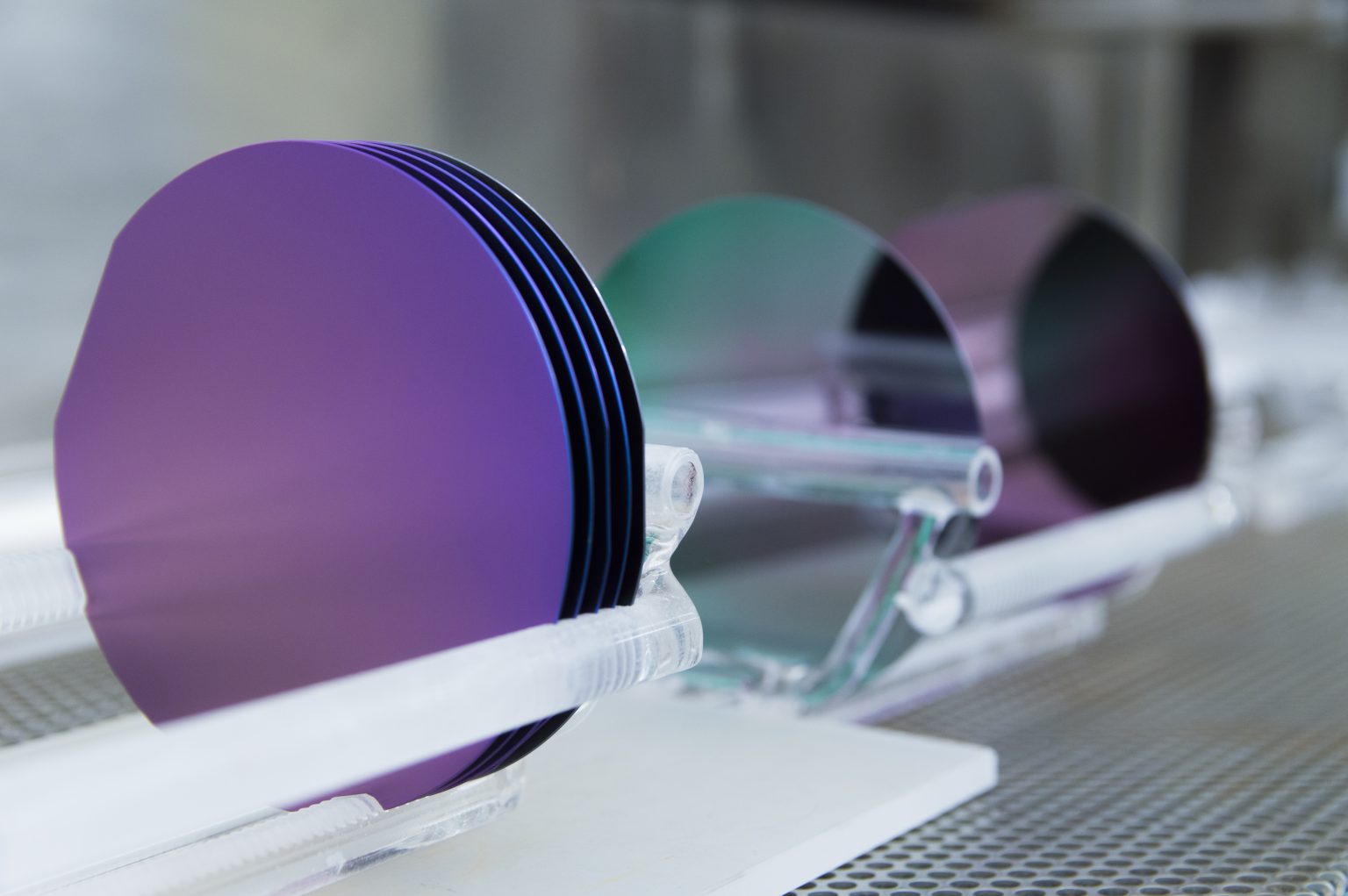 This is a set of 100 mm silicon wafers grown in a cleanroom facility.  They are sitting in quartz holders or boats after being in a silicon dioxide growth furnace.  The high heat from the furnace combined with oxygen converts the surface of the wafers to silicon dioxide.  The wafer colors are dictated by the thickness of the silicon dioxide layer and the viewing angle.  The purples and greens shown on these wafers are quite common and give the cleanroom a colorful and artistic touch.